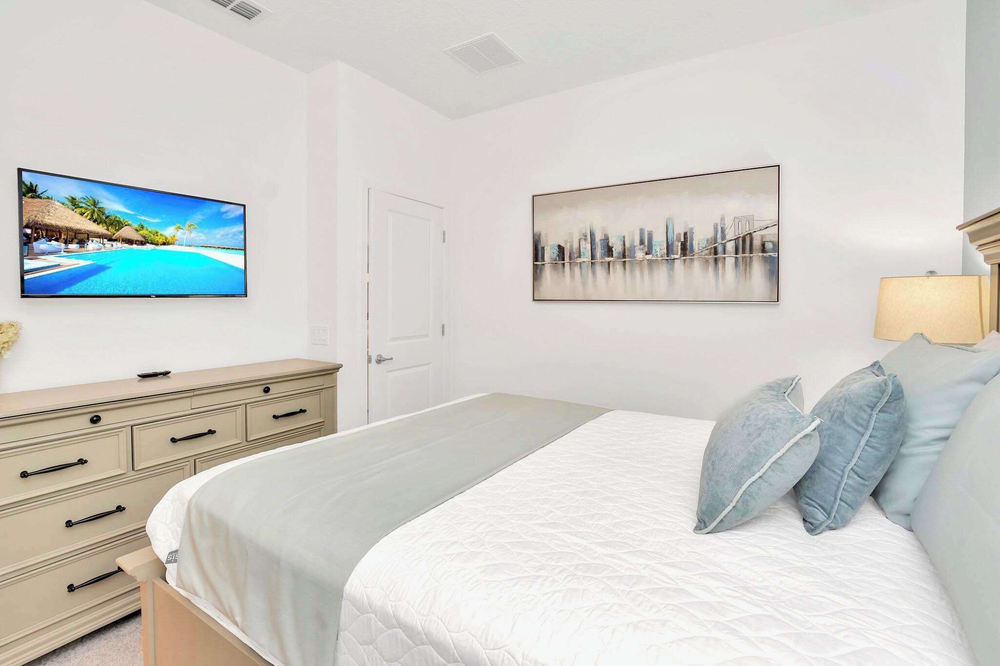 A bedroom with a bed, a dresser, a television, and two wall-mounted paintings.