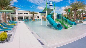 A pool area with a water slide, lounge chairs, and a building in the background.
