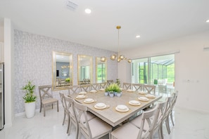 A dining area with a large table set for six, surrounded by chairs, with a modern chandelier above.