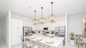 Una cocina moderna con armarios blancos, una isla central con asientos e iluminación colgante.
