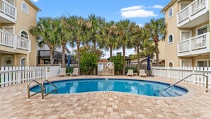 A swimming pool with a brick deck, surrounded by palm trees and a white fence.