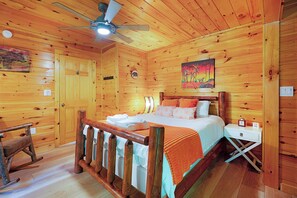 A wooden cabin bedroom with a bed, a rocking chair, a nightstand, and a ceiling fan.