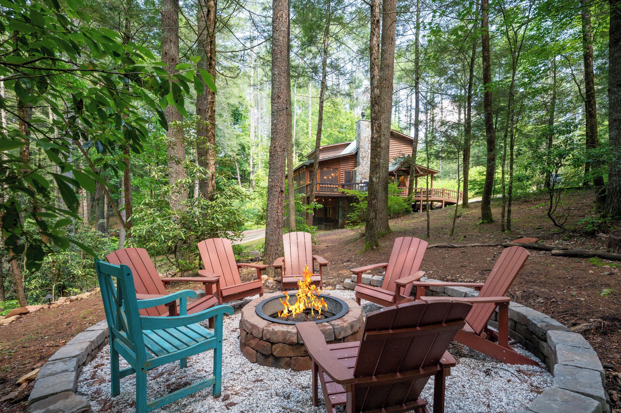 Un décor forestier avec un foyer entouré de fauteuils Adirondack, un chalet en arrière-plan et un foyer en pierre.