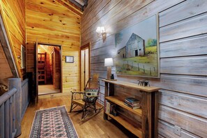 A wooden interior with a rocking chair, a bookshelf, and a painting of a barn.