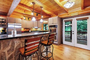 A kitchen with wooden cabinets, a stone island, and bar stools. - Mountaintown Creek Lodge - Ellijay GA (Ellijay)