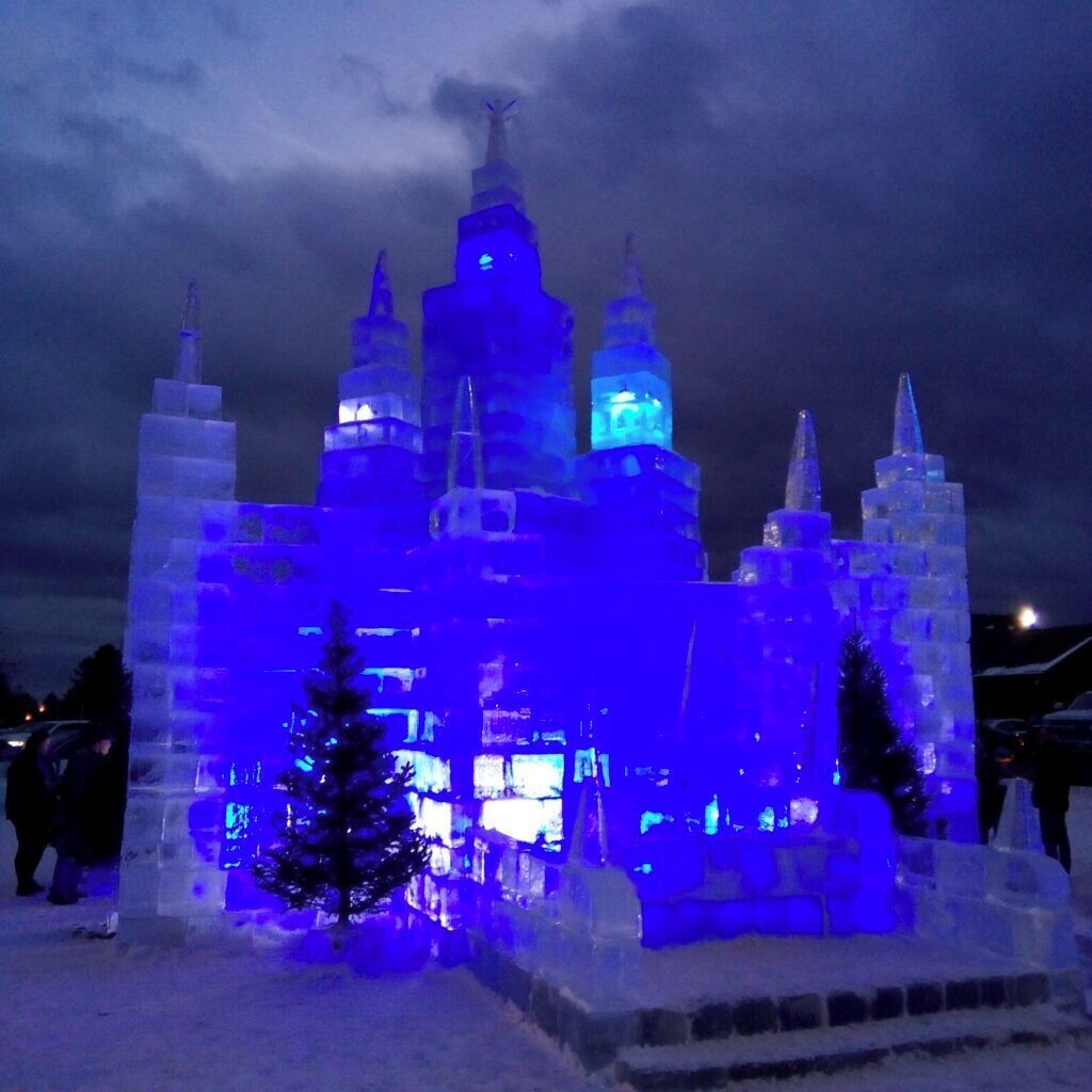 An ice sculpture resembling a castle with illuminated blue lights, surrounded by snow.