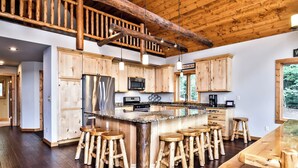 A spacious kitchen with wooden cabinets, a large island with stools, a wooden staircase, and a view of the outdoors. - NEW! Gorgeous Northwoods Home on the Eagle River Chain of Lakes (Eagle River)
