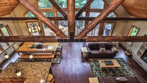 A spacious loft-style living area with a high ceiling, exposed wooden beams, a large dining table, and a cozy seating area with a sofa and armchairs. - NEW! Gorgeous Northwoods Home on the Eagle River Chain of Lakes (Eagle River)