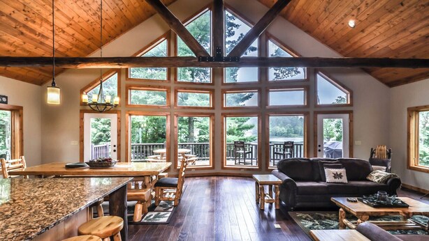 A spacious room with a high ceiling, large windows, a wooden dining area, and a cozy seating area with a couch and coffee table. - NEW! Gorgeous Northwoods Home on the Eagle River Chain of Lakes (Eagle River)