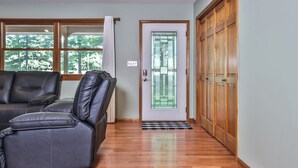 A room with a wooden floor, a leather sofa, a glass door with a geometric pattern, and a view of trees through a window.