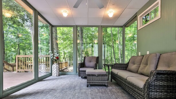 A sunroom with large windows, wicker furniture, and a view of a wooded area.