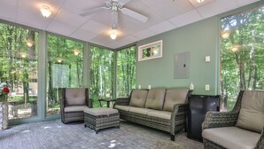 A room with wicker furniture, large windows, and a ceiling fan.