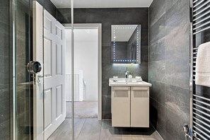 A modern bathroom with a glass door, a vanity with a mirror, and a towel rack. - 2 Bedroom Service Apt in Artillery Lane (London)