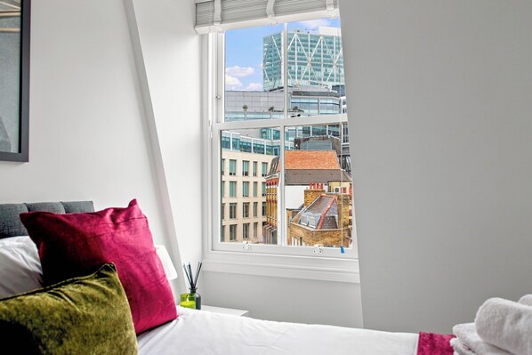 A bedroom with a large window, a bed with white bedding, and a red pillow. - 2 Bedroom Service Apt in Artillery Lane (London)