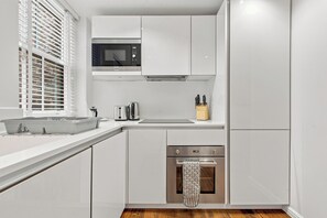 A modern kitchen with white cabinetry, a built-in microwave, a toaster, and a stainless steel oven. - 2 Bedroom Service Apt in Artillery Lane (London)