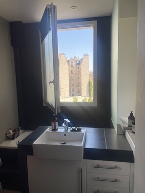 A modern bathroom with a large window, a sink, and a mirror.