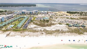 An aerial view of a coastal hotel area with multiple buildings, a sandy beach, and a parking lot.