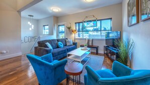 A modern living room with a blue sofa, a coffee table, and a TV. There is a window with a view of the city. - Hull Street Loft 2 Bedroom Townhouse by RedAwning (Hood River)