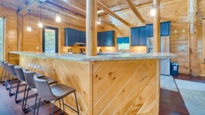 A wooden cabin interior with a kitchen area, bar stools, and a large window. - Sensational Views 4 Bedroom Cabin by Heavenly Views Resort (Gatlinburg)
