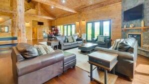 A spacious living room with wooden beams, leather sofas, a stone fireplace, and large windows. - Sensational Views 4 Bedroom Cabin by Heavenly Views Resort (Gatlinburg)