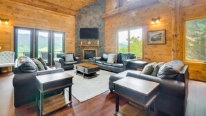 A spacious living room with wooden walls and large windows, furnished with leather sofas and tables, and a fireplace. - Sensational Views 4 Bedroom Cabin by Heavenly Views Resort (Gatlinburg)
