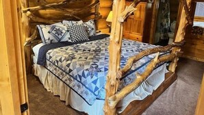 Ein rustikales Schlafzimmer in einer Holzhütte mit einem Himmelbett, einer gesteppten Bettdecke und einer Holzbalkendecke.