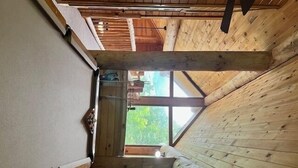 Eine Holzhütte mit hohen Decken, einem geneigten Dach, einem großen Fenster und Blick ins Freie.