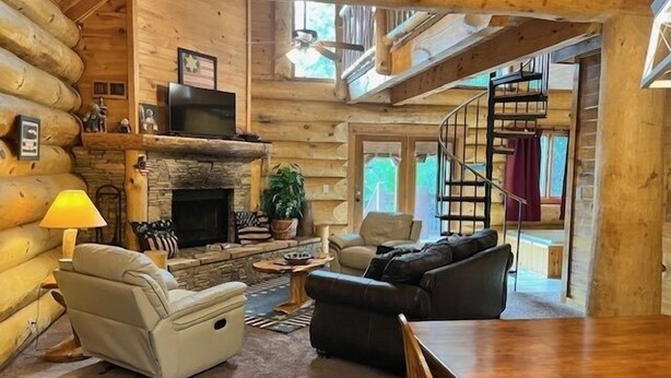 Ein gemütliches Blockhaus-Interieur mit Kamin, einer Couch, einem Esstisch und einer Treppe, die in ein Obergeschoss führt.