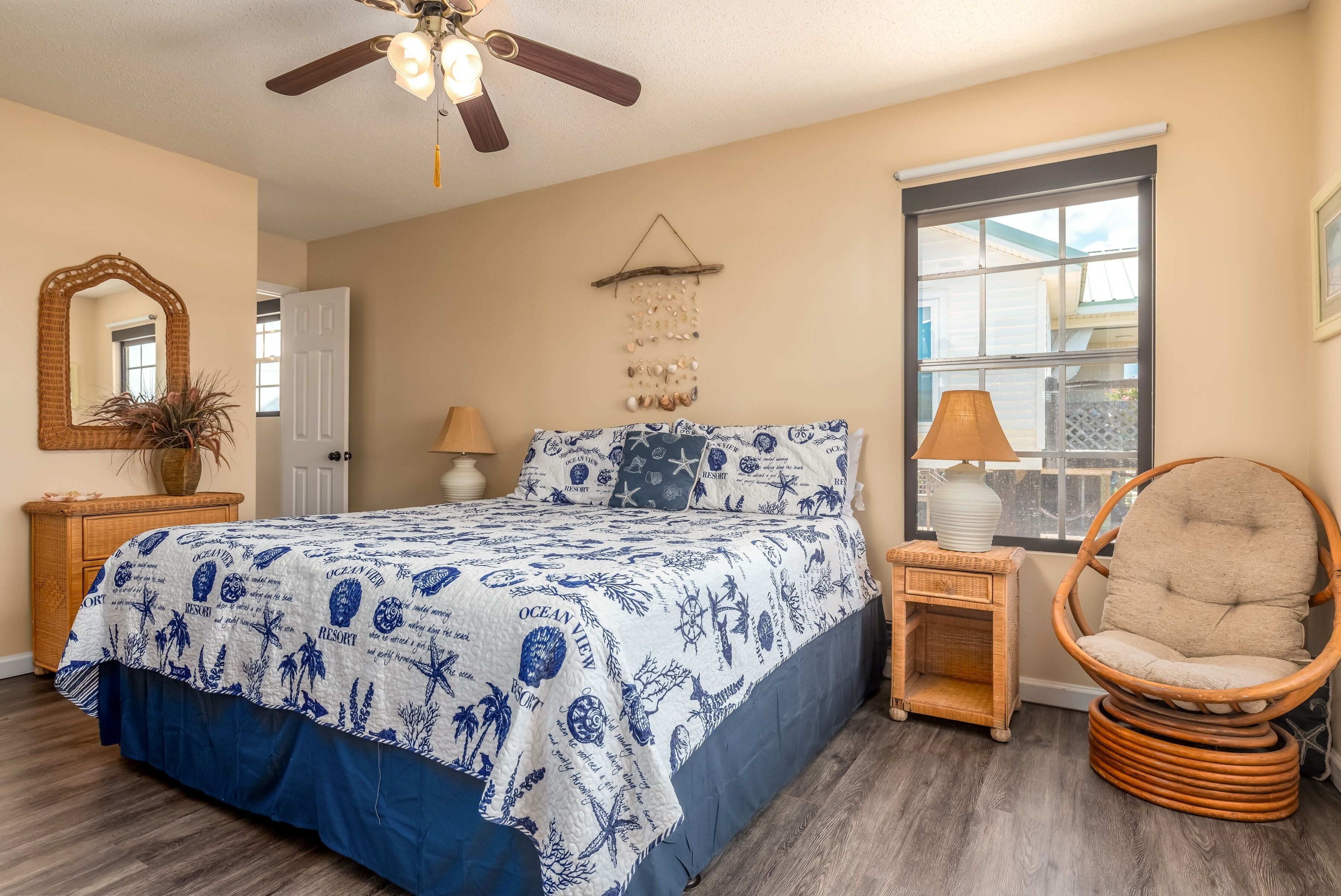A bedroom with a bed, a chair, a ceiling fan, a window, and a wall-mounted decoration.