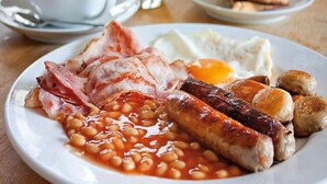 En frukosttallrik med bacon, korv, bönor, ägg och rostat bröd.