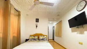 Ett hotellrum med en säng, en takfläkt, en klocka och en tv som är monterad på väggen.