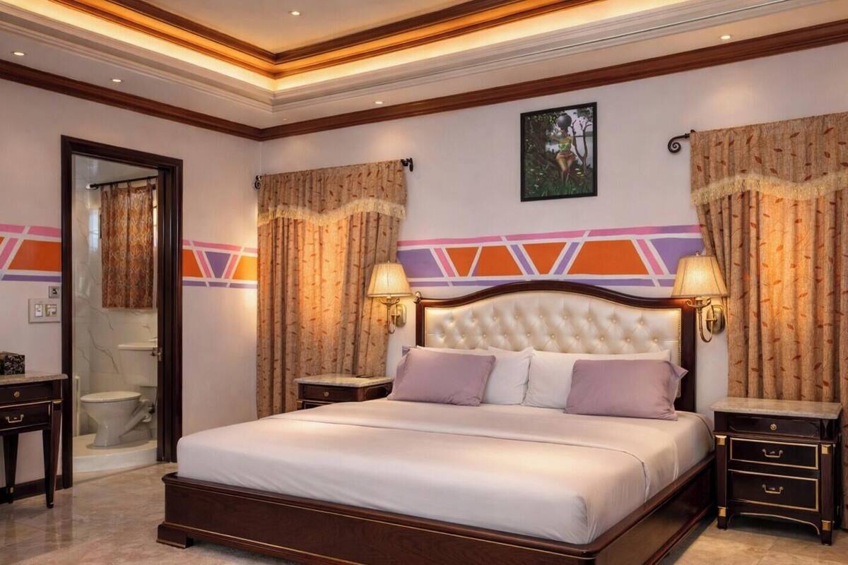 A bedroom with a large bed, two bedside tables, a headboard, and a wall-mounted lamp.