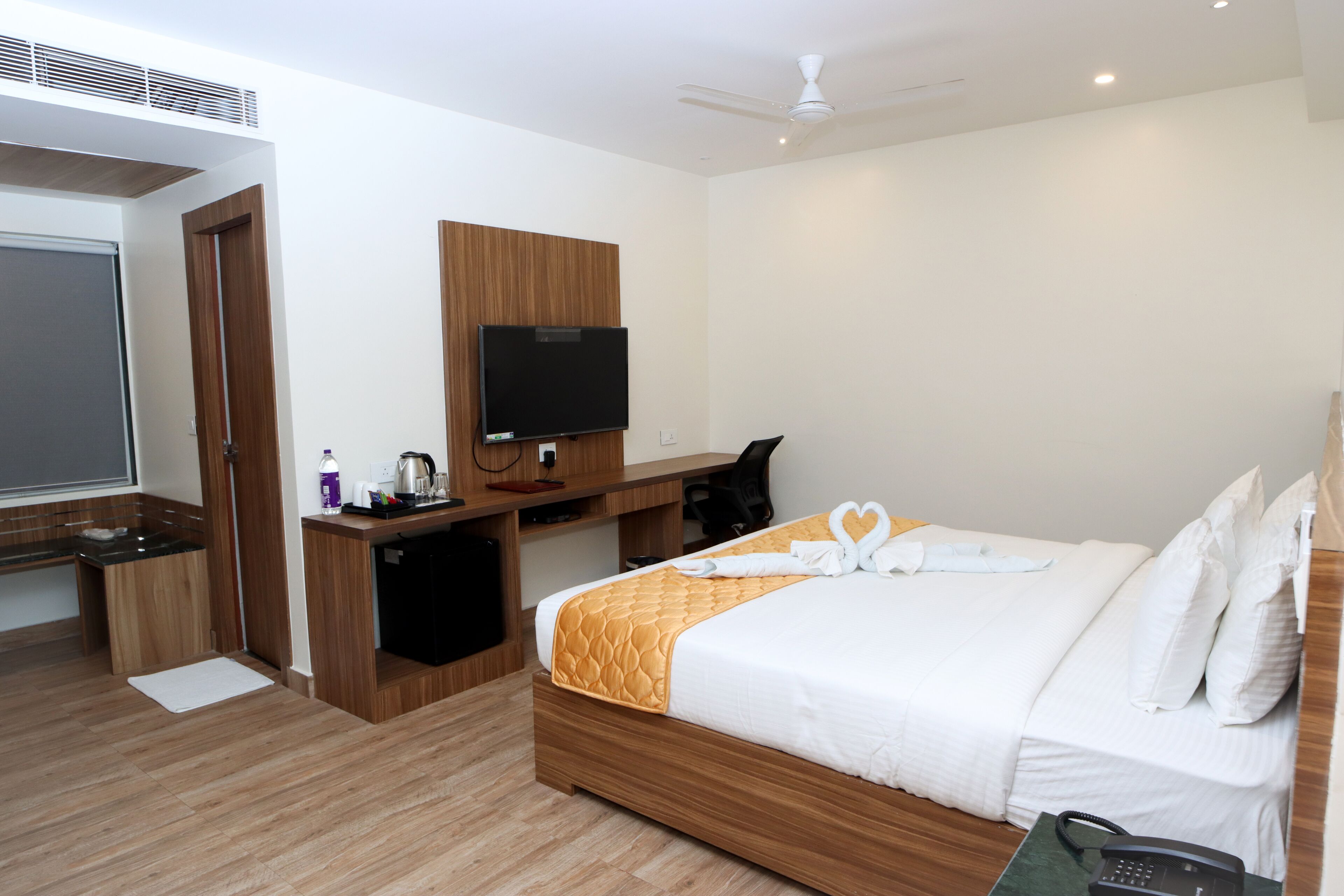 Ein Hotelzimmer mit Bett, Schreibtisch, Fernseher und Deckenventilator.