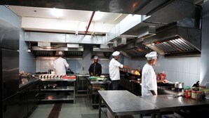 A professional kitchen with stainless steel surfaces, multiple cooking stations, and overhead ventilation. - Hotel Sharda Residency (Patna)