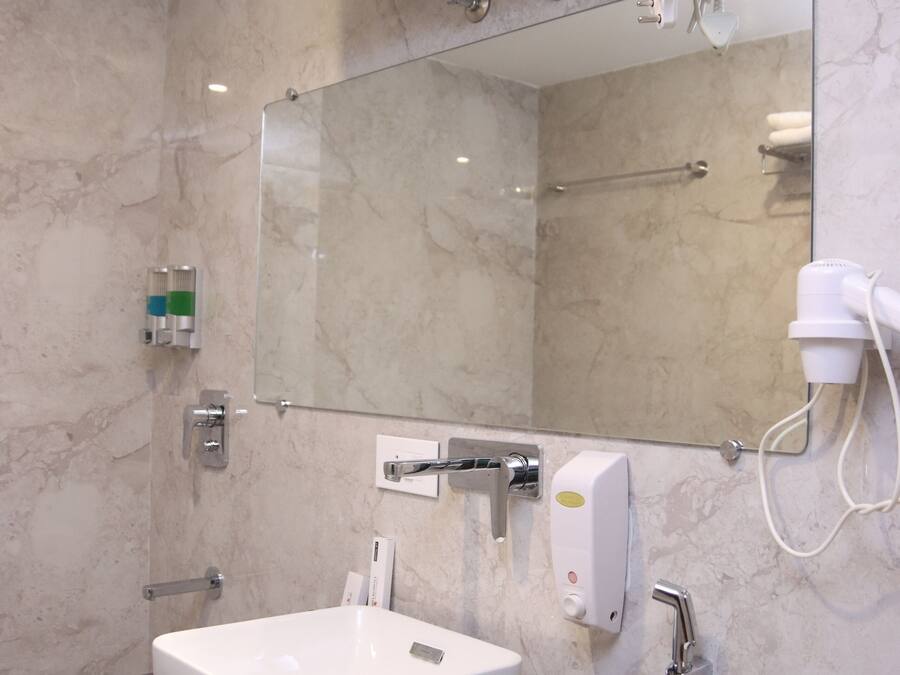 Ein modernes Badezimmer mit Marmorwand, Waschbecken in Weiß, einem Spiegel und einer Duschbrause.