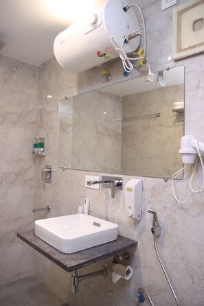 A modern bathroom with a marble wall, a white sink, a mirror, and a handheld showerhead. - Hotel Sharda Residency (Patna)