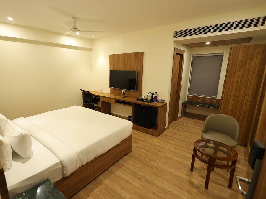 A hotel room with a bed, desk, chair, television, and a window.