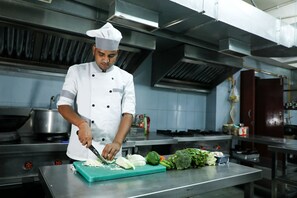 Un chef en una cocina profesional con superficies de acero inoxidable, una amplia tabla de cortar y diversos vegetales.