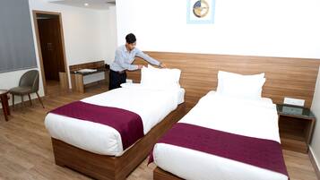 Quarto de hotel com duas camas, uma escrivaninha, uma cadeira e uma mesinha.
