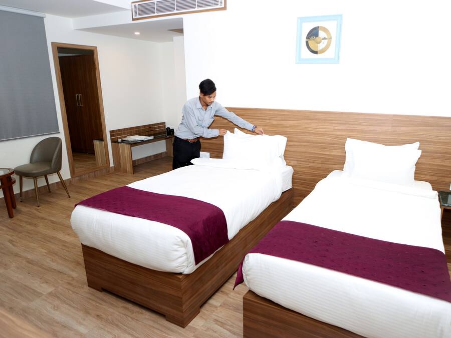 Quarto de hotel com duas camas, uma escrivaninha, uma cadeira e uma mesinha.