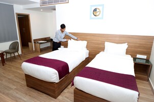 Quarto de hotel com duas camas, uma escrivaninha, uma cadeira e uma mesinha.