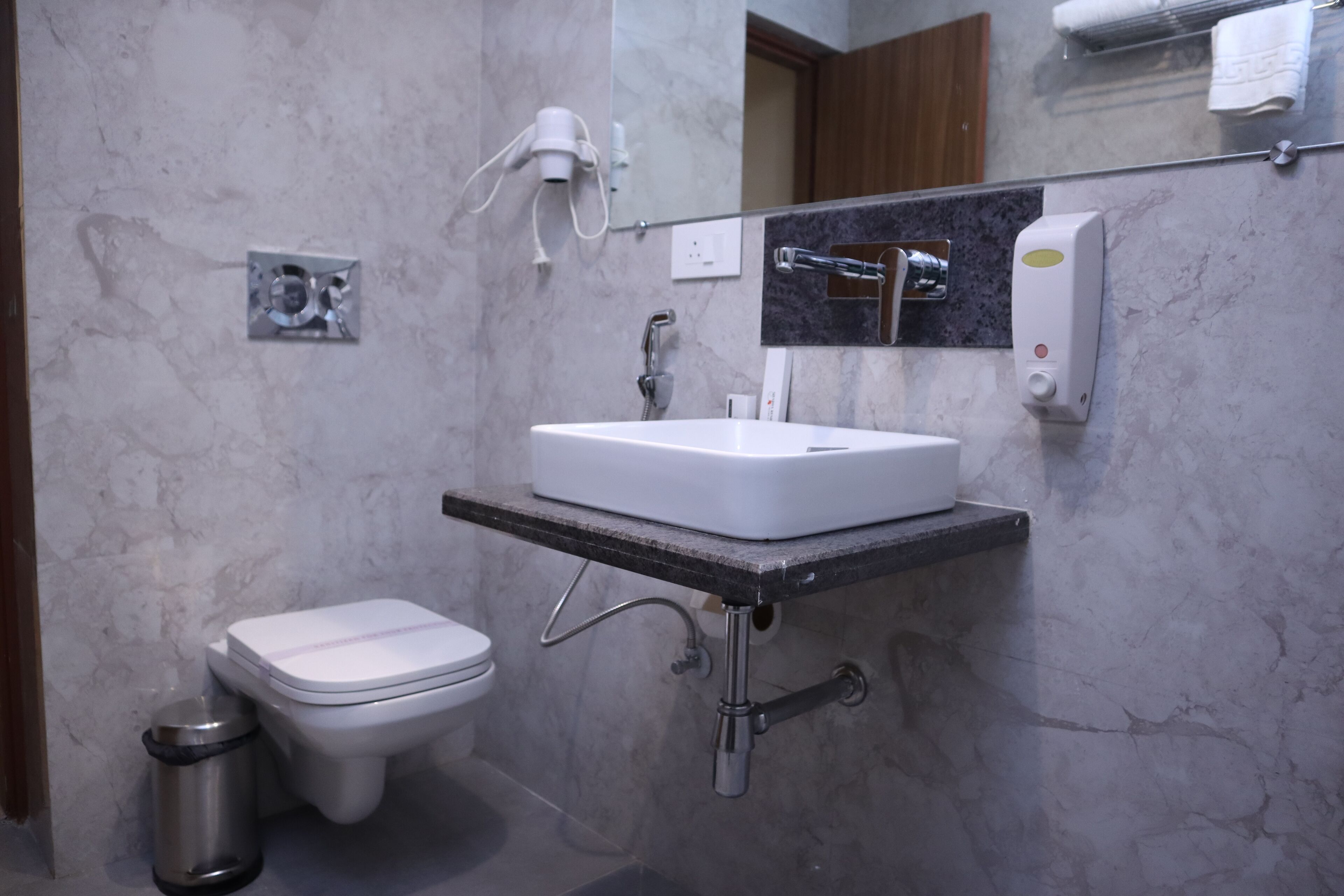 A bathroom with a white sink, a toilet, a trash can, a hairdryer, and a soap dispenser.