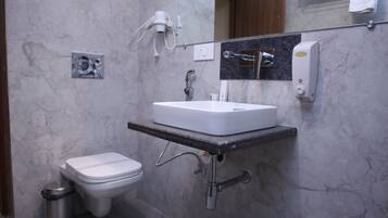 Un baño con lavamanos blanco, inodoro, un cubo de basura, secador de pelo y dispensador de jabón.