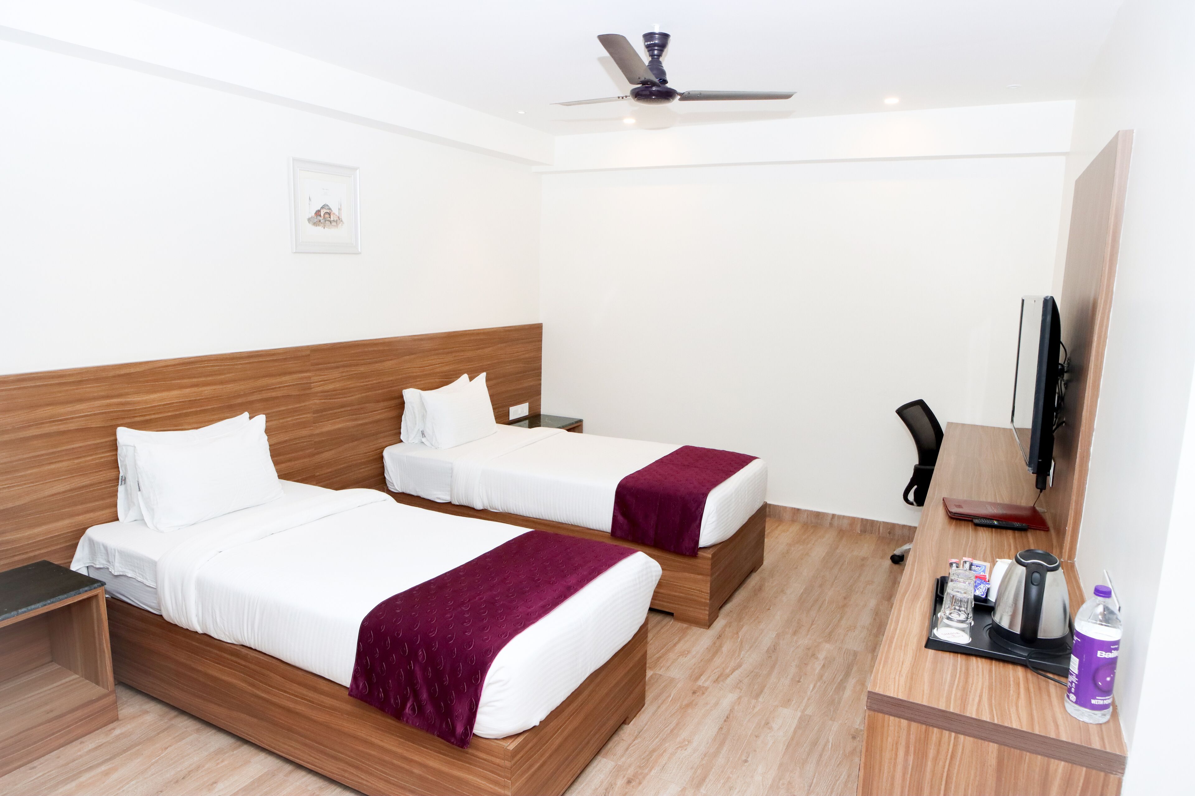Habitación de hotel con dos camas, un escritorio con computadora, una cafetera y una botella de agua.
