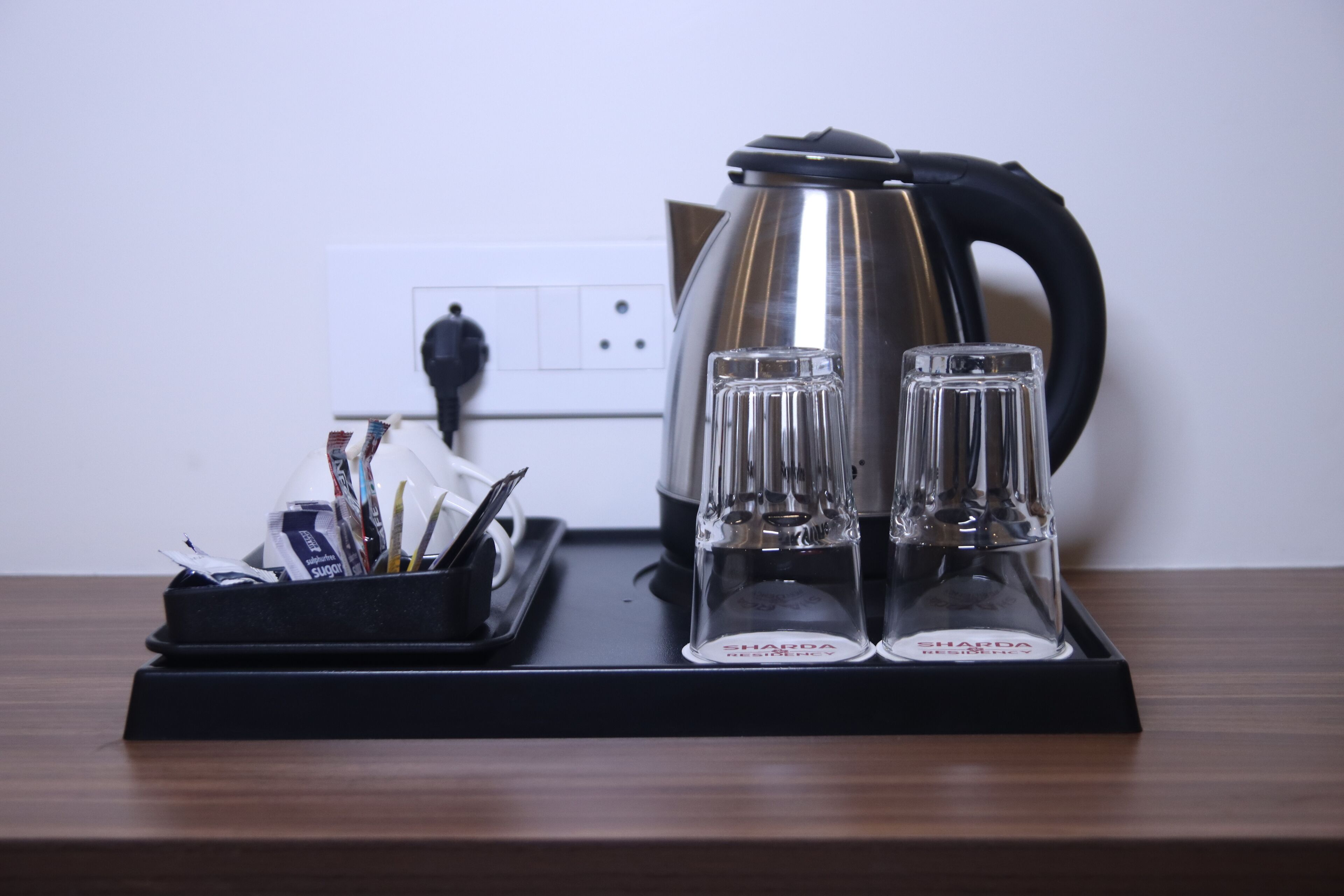 A kitchen counter with a kettle, two glasses, and a tray with utensils.