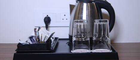 A kitchen counter with a kettle, two glasses, and a tray with utensils.