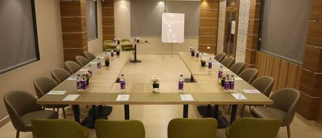 Un salón de conferencias con una larga mesa, sillas, una pizarra y botellas de agua.