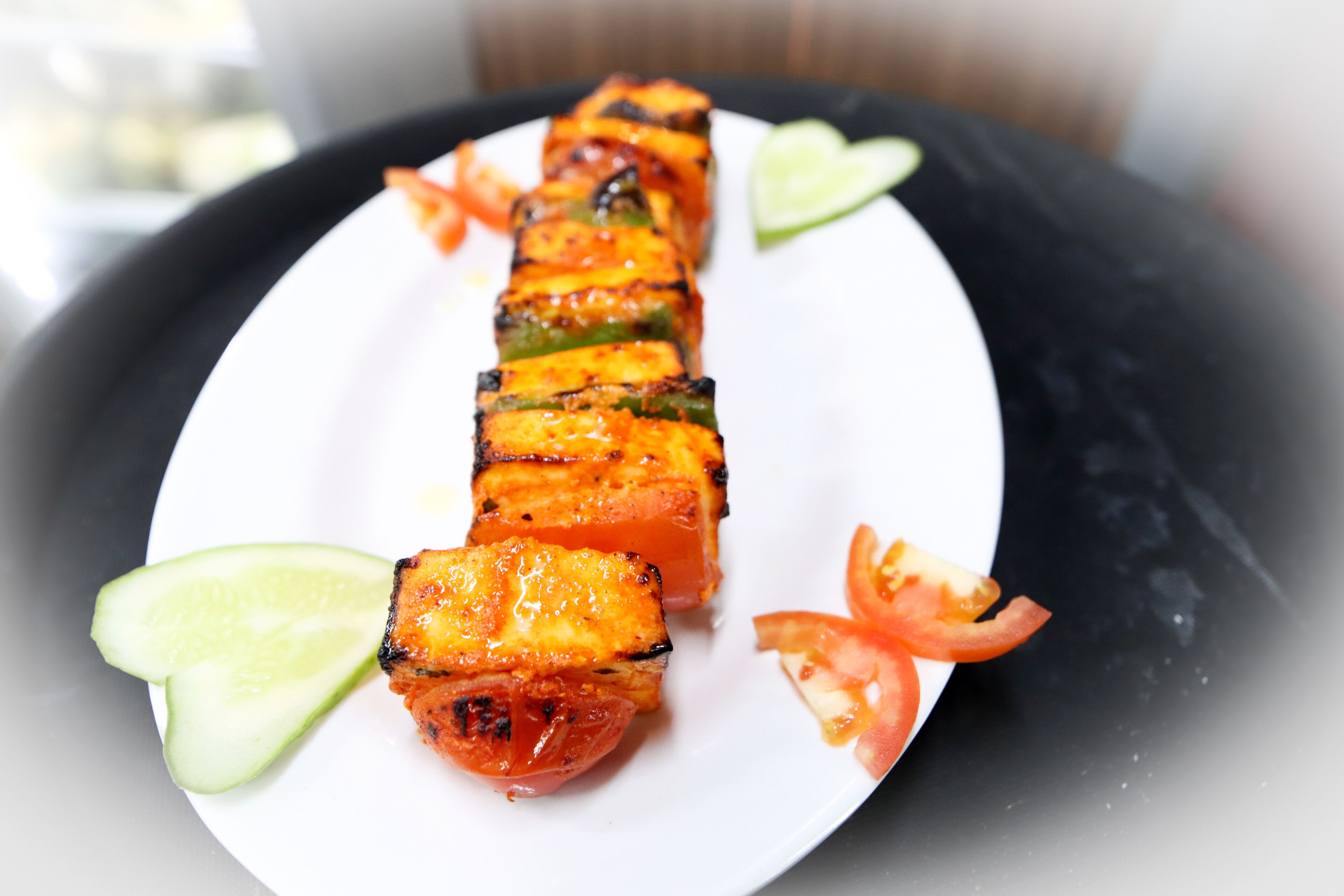 A plate with grilled vegetable skewers, garnished with cucumber and tomato slices.