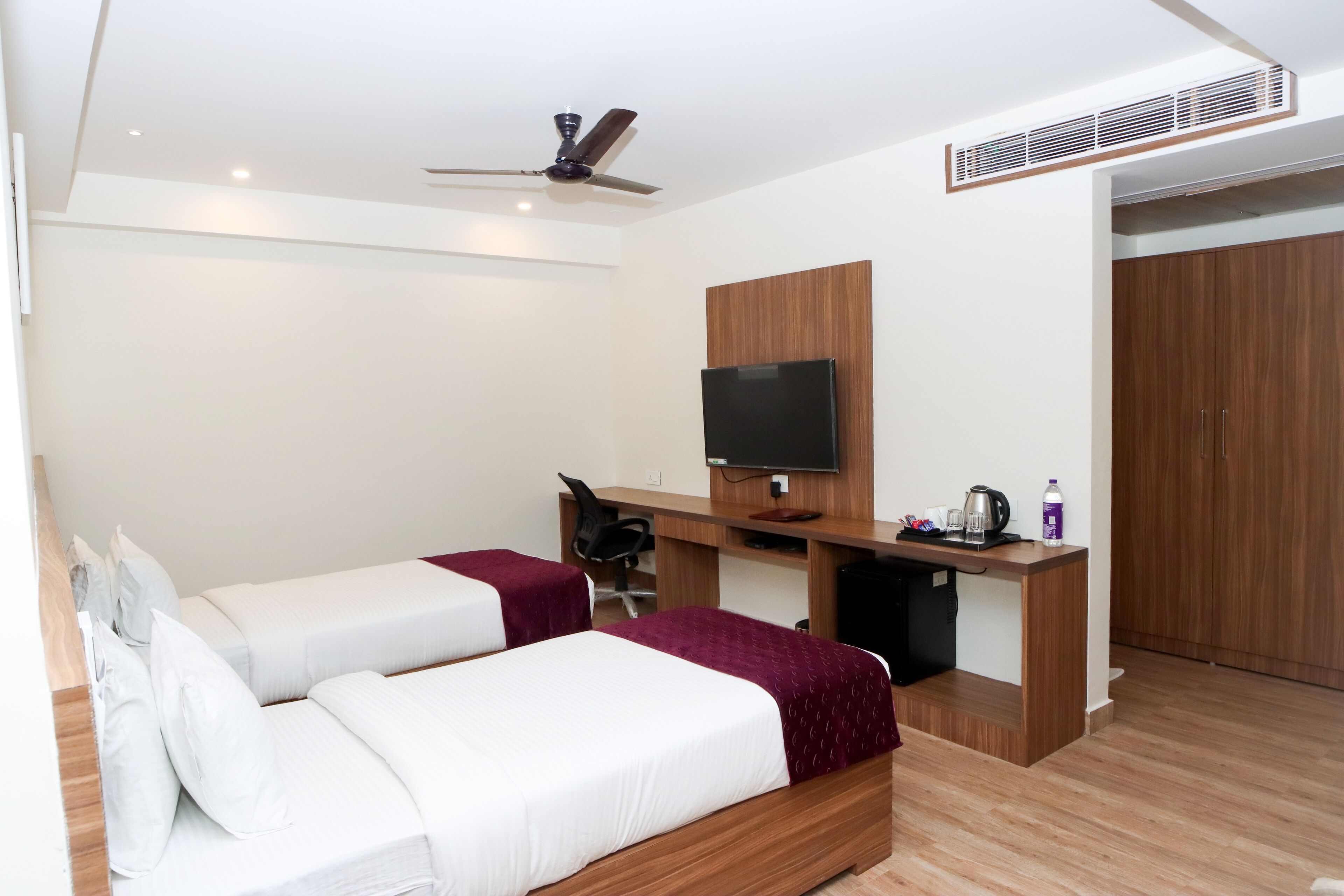 Een hotelkamer met twee bedden, een bureau met een televisie, een plafondventilator en een kledingkast.