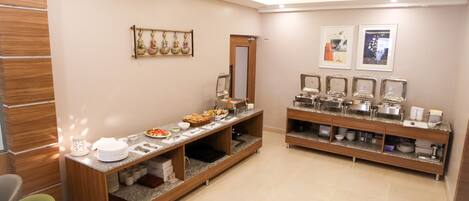 A modern hotel room with a wooden reception desk, a buffet counter with various food items, and a mirror on the wall.